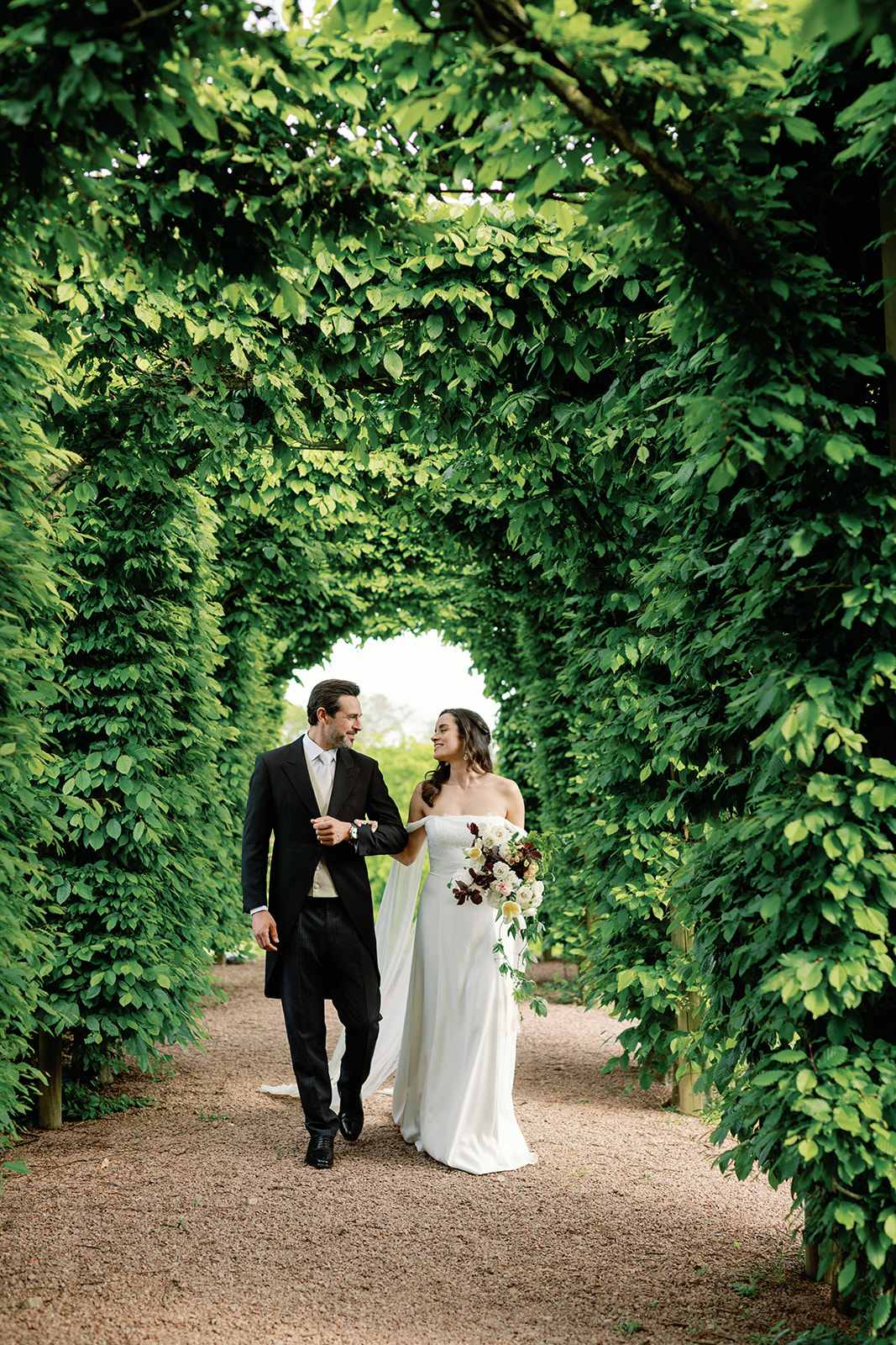 Couple walking through hornbeam arches